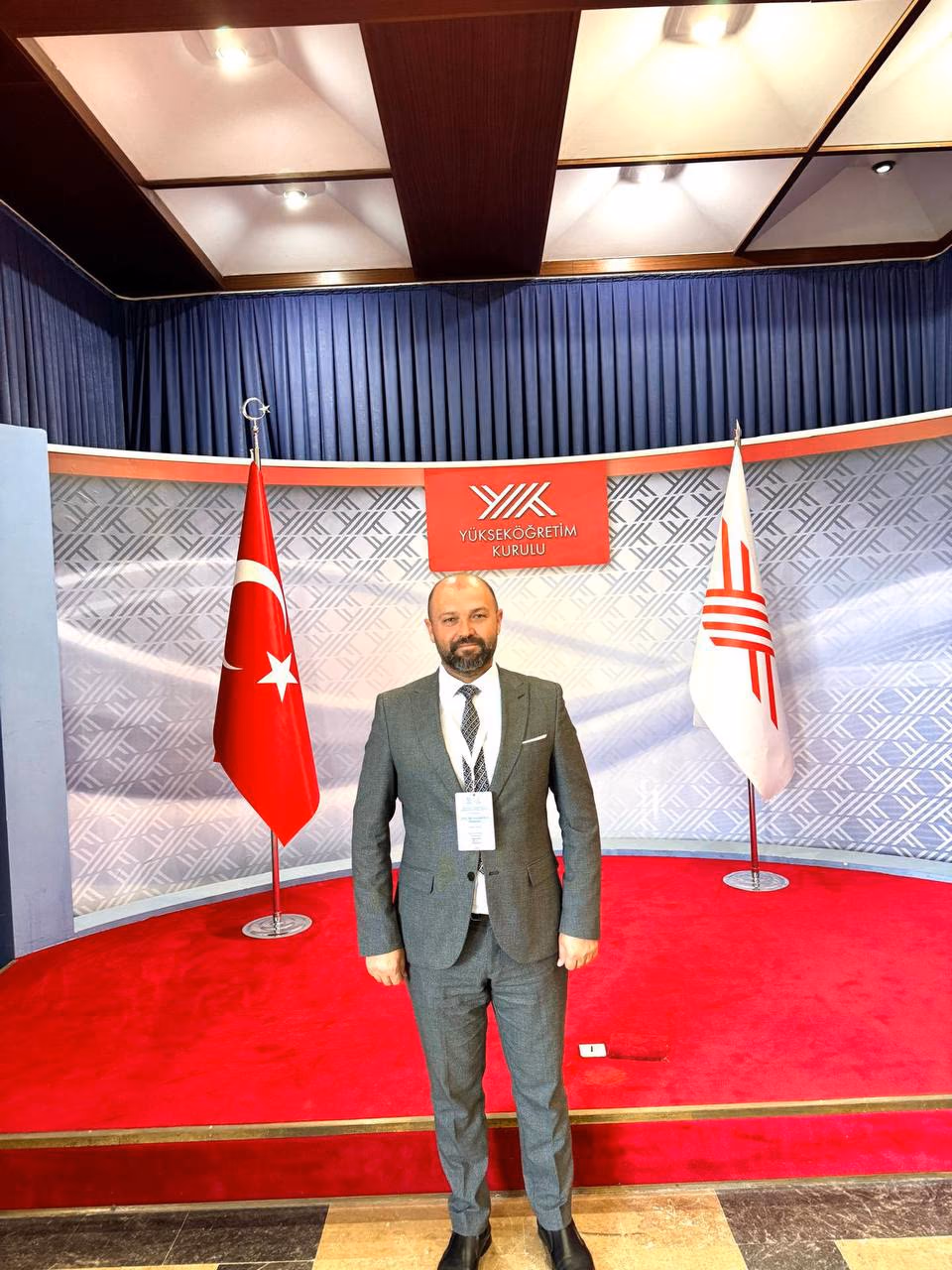 Doç. Dr. Muharrem Özdemir, Yükseköğretim Kurulu (YÖK) ziyaretinde Türk bayrağı ve YÖK forsu önünde