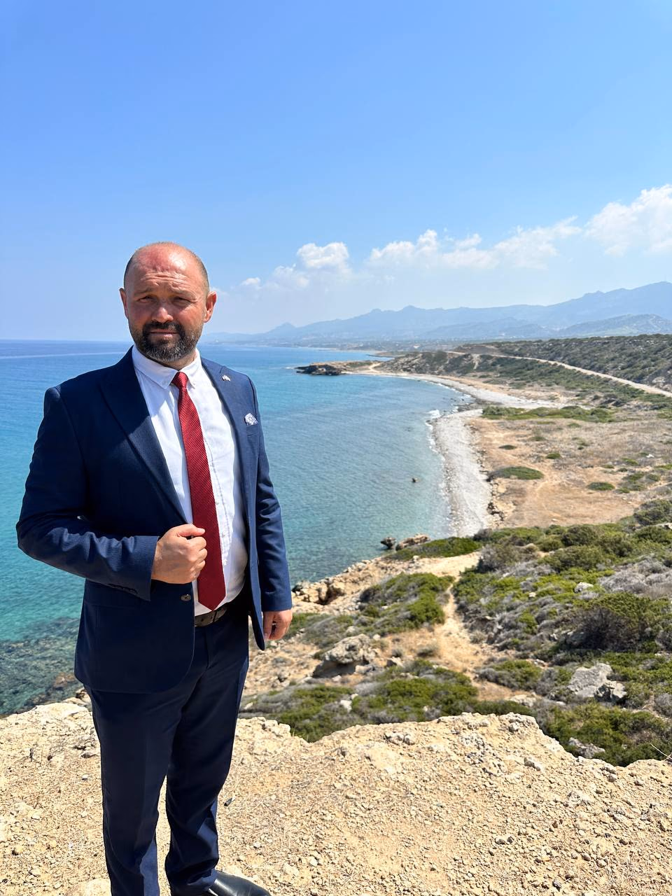 Doç. Dr. Muharrem Özdemir, falez üzerinde — arkada turkuaz sahil şeridi