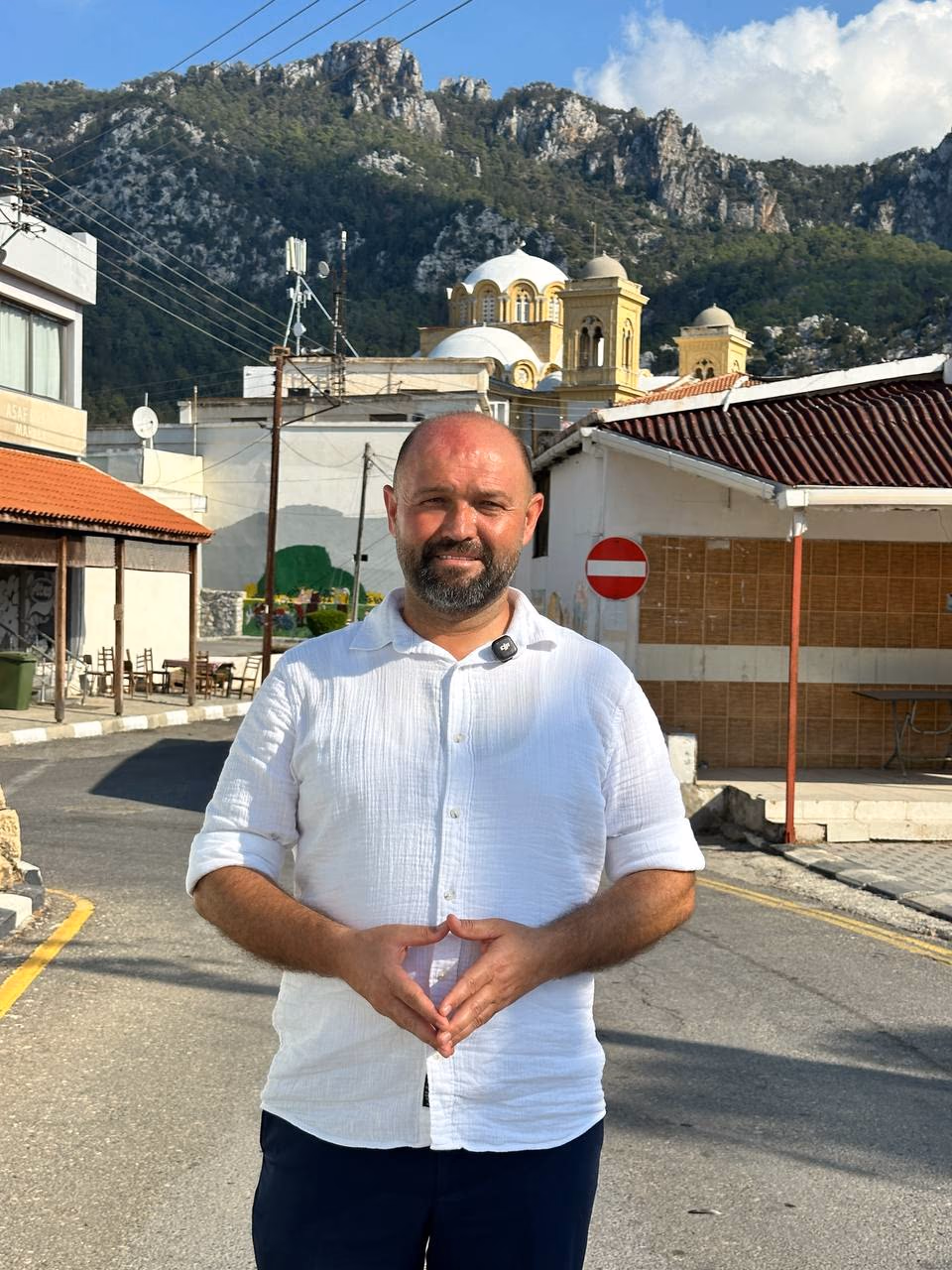 Doç. Dr. Muharrem Özdemir, Aktunç Mahallesi'nde Tatlısu belde merkezinde — arkada Tatlısu Camii ve Beşparmak Dağları